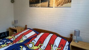 Ein Schlafzimmer mit einem hölzernen Bett, einer weißen Ziegelwand und drei gerahmten Bildern vom Strand.