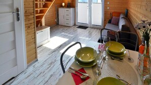 L’intérieur chaleureux d’un chalet comprend un coin repas aménagé pour quatre personnes, un escalier, un canapé et un petit meuble.
