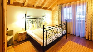A bedroom with a wooden ceiling, a metal bed frame, a bedside table, a chair, and a window with curtains. - Chalet in Kitzbuhel Alps Near Hiking Trails (Wildschönau)