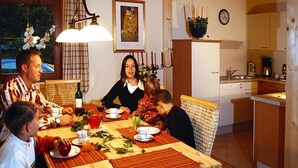 A family dining at a wooden table with placemats, surrounded by wicker chairs. A chandelier hangs above, and a framed painting is on the wall. - Chalet in Kitzbuhel Alps Near Hiking Trails (Wildschönau)