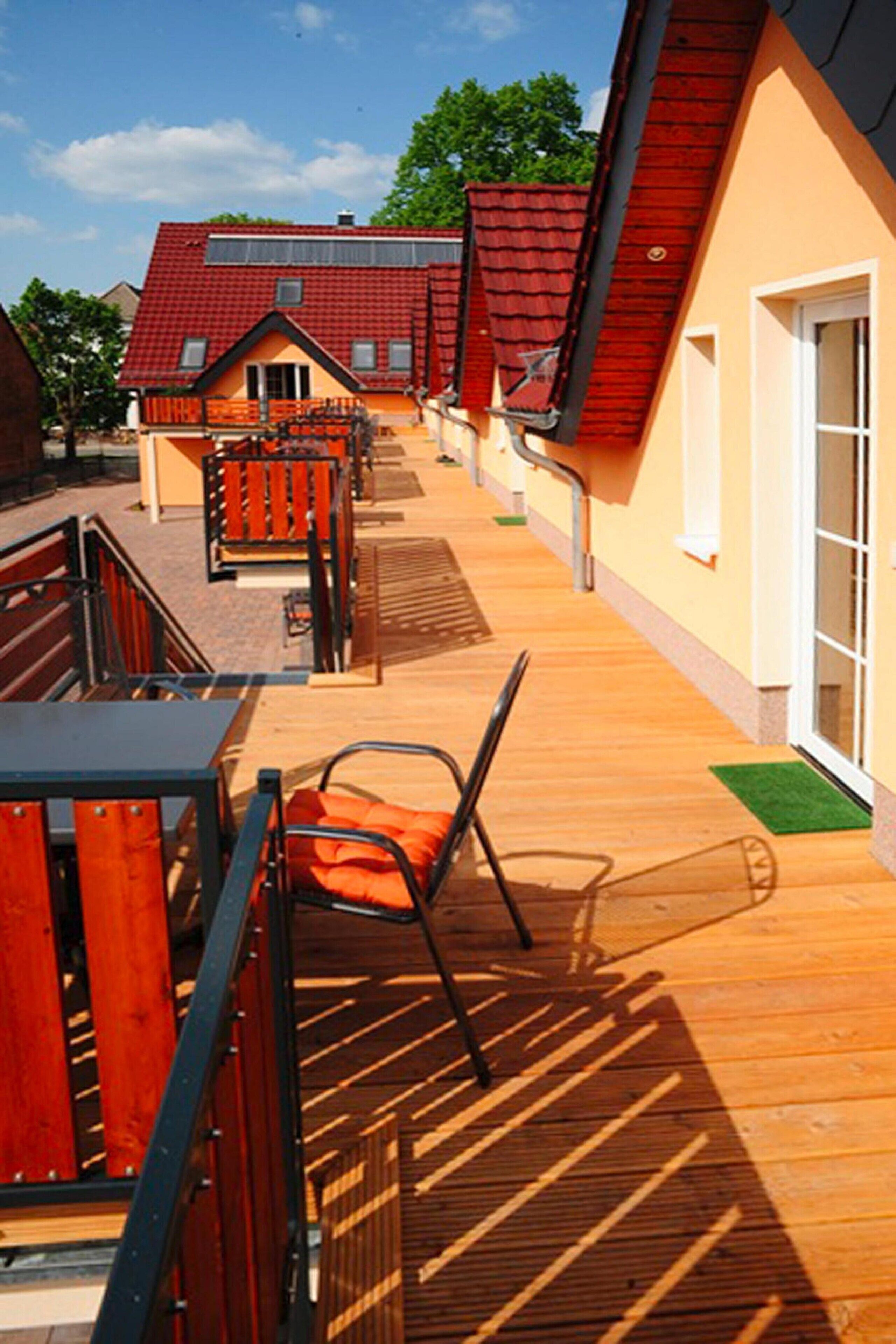 Una terraza de madera con mobiliario exterior y vistas a un edificio de techo rojo.