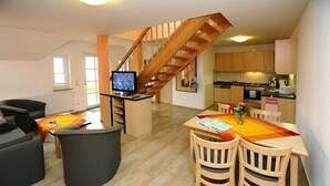 A modern kitchen with wooden cabinets, a dining area with a table and chairs, and a staircase leading to an upper level. - Apartment on the Spree River in Schlepzig (Schlepzig)