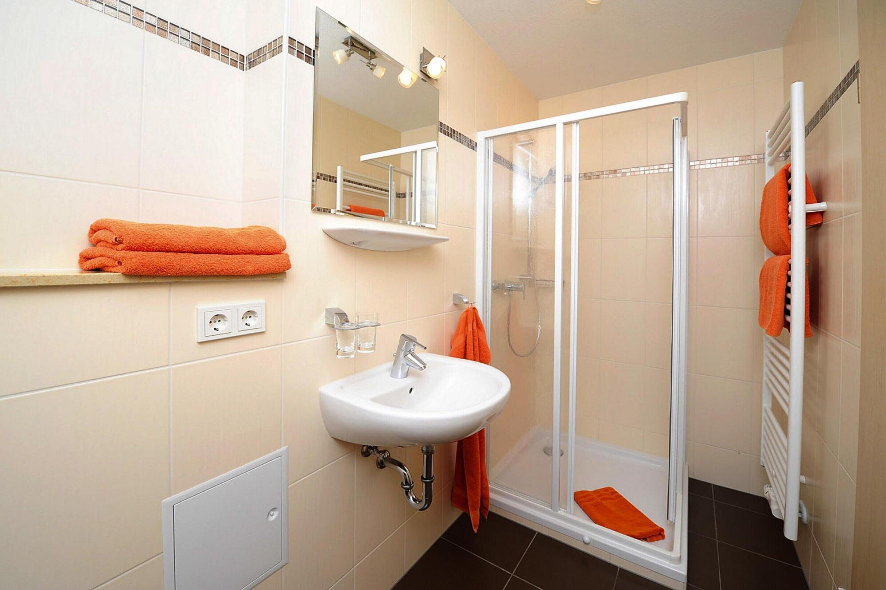 A bathroom with a sink, mirror, shower, and orange towels.