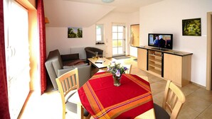 A cozy living room with a sofa, a dining table with a red tablecloth, and a television on a stand. - Apartment on the Spree River in Schlepzig (Schlepzig)