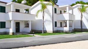 A modern two-story building with a flat roof, white exterior walls, and green shutters. There are two palm trees in front of the building. - Bungalow in a Resort in Lido del Sole With Terrace (Rodi Garganico)