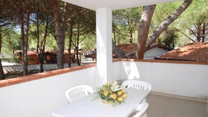 A covered outdoor dining area with a table and chairs, surrounded by trees and a white wall. - Bungalow in a Resort in Lido del Sole With Terrace (Rodi Garganico)