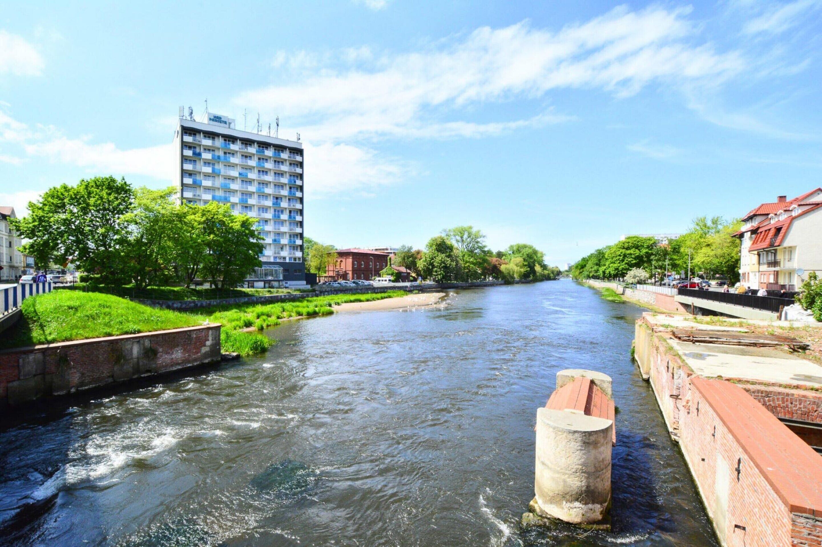 Un río con un puente, un edificio alto y vegetación a lo largo de las orillas.