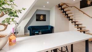 Un interior moderno con una mesa blanca, un sofá azul, una escalera de madera y una planta en maceta.