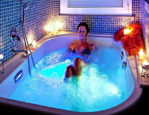 Una mujer se relaja en un jacuzzi, con un panel de control, rodeada de paredes de azulejos y velas.