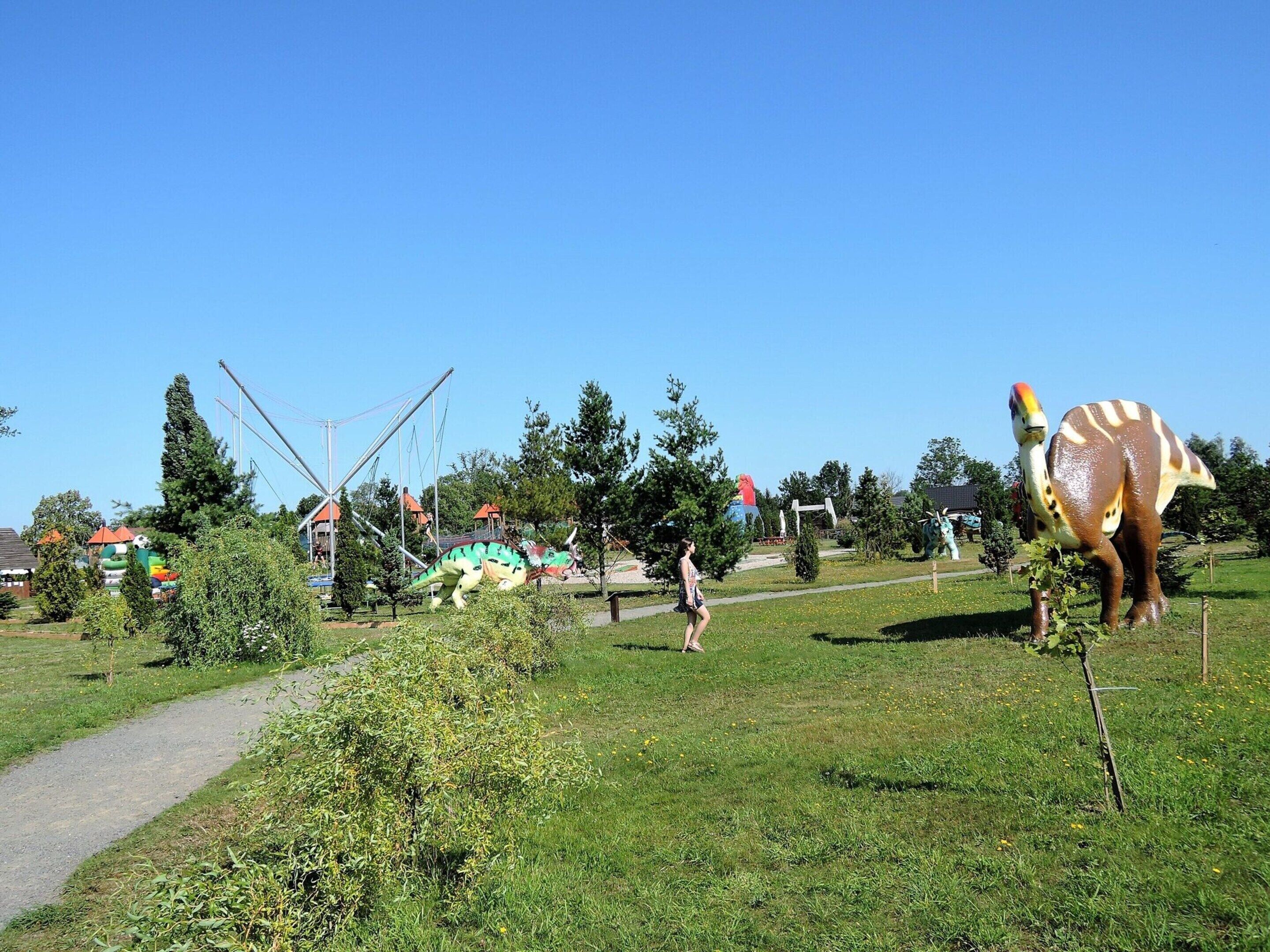 Ein Park mit einer großen Dinosaurier-Statue, einem Spielplatz und blauem Himmel.