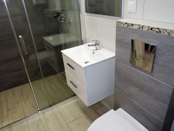 Un baño moderno con cabina de ducha de vidrio, tocador blanco con lavabo y espejo con marco decorativo.
