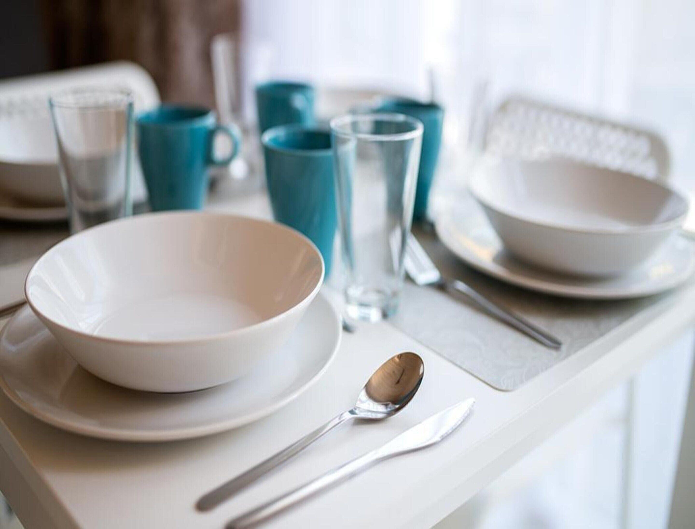 A dining table with white plates, a bowl, a spoon, and a knife.