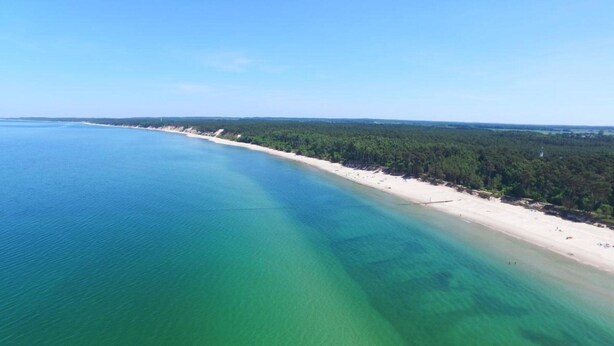 Vista aérea de una playa con aguas turquesas cristalinas y una orilla arenosa.