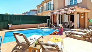 A pool area with lounge chairs, a table, and a covered seating area. - Holiday Home Meloneras Hills, Meloneras (San Bartolomé de Tirajana)