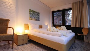 Siististi järjestetty hotellihuone, jossa on sänky, yöpöydät, tuoli ja ikkuna, jossa on verhot.
