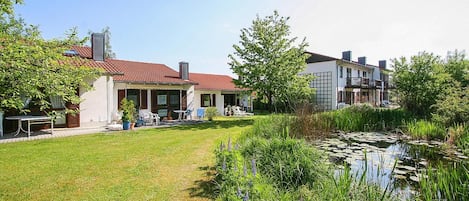 A residential property with a well-maintained lawn, a pond with lily pads, and a patio area with outdoor furniture.