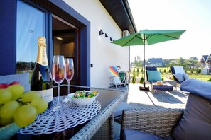 An outdoor seating area with wicker furniture, a table with a bottle of wine and glasses, and a green umbrella. - Terraced House in Mielenko Near Seaside Beach (Mielno)