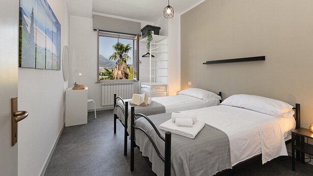 Ein modernes Hotelzimmer mit zwei Betten, einem Fenster mit Blick auf Palmen, einem weißen Schrank und einem Bild an der Wand.