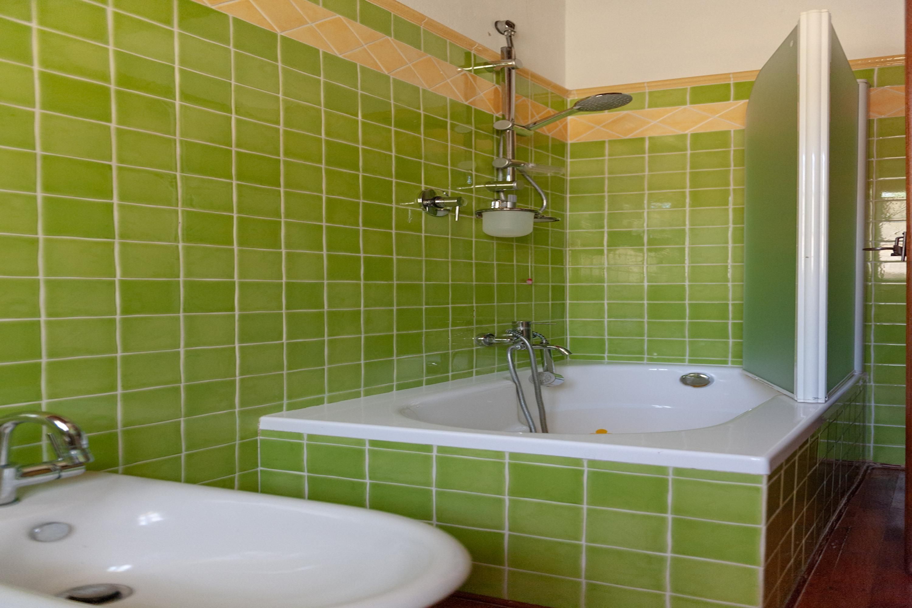 Casa de banho com paredes azulejadas em tons de verde, uma banheira branca e uma pia branca.