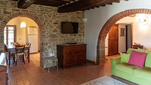 Un espace repas agrémenté d’un mur en pierre, de poutres en bois au plafond, d’une table à manger en bois avec des chaises, et d’une chaise en verre transparent.