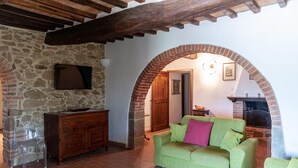 Un salon chaleureux avec un mur en pierre, un plafond en bois, un canapé vert, un meuble en bois et une cheminée.