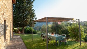 Un espace de restauration en plein air agrémenté d’une pergola, d’un bâtiment en pierre et d’une végétation luxuriante.