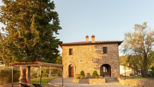 Un bâtiment en pierre avec un toit en tuiles, un espace extérieur couvert avec des sièges et une pelouse bien entretenue.