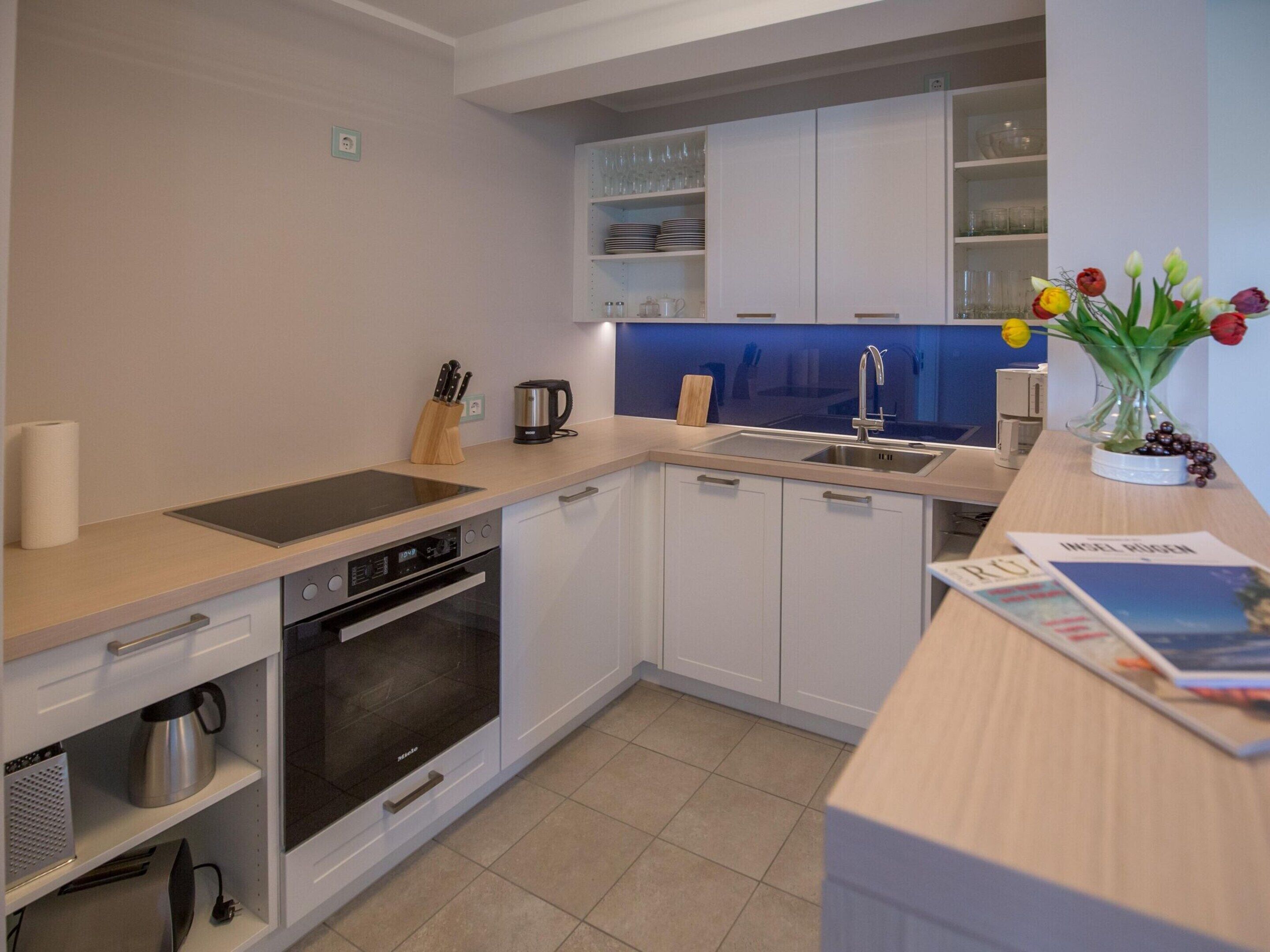 A modern kitchen with white cabinets, a built-in oven, a sink, and a coffee maker.