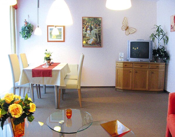 A dining area with a table, chairs, a glass-top table, a vase with flowers, a framed picture, a television on a cabinet, and a butterfly decoration on the wall. - Apartment in Cuxhaven mit Gemeinschaftspool (Cuxhaven)