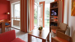 A living room with a sofa, a coffee table, a bookshelf, and a TV. - Apartment in Cuxhaven mit Gemeinschaftspool (Cuxhaven)