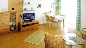 A living room with a television, dining table, chairs, and a wicker chair. - Apartment in Cuxhaven mit Gemeinschaftspool (Cuxhaven)