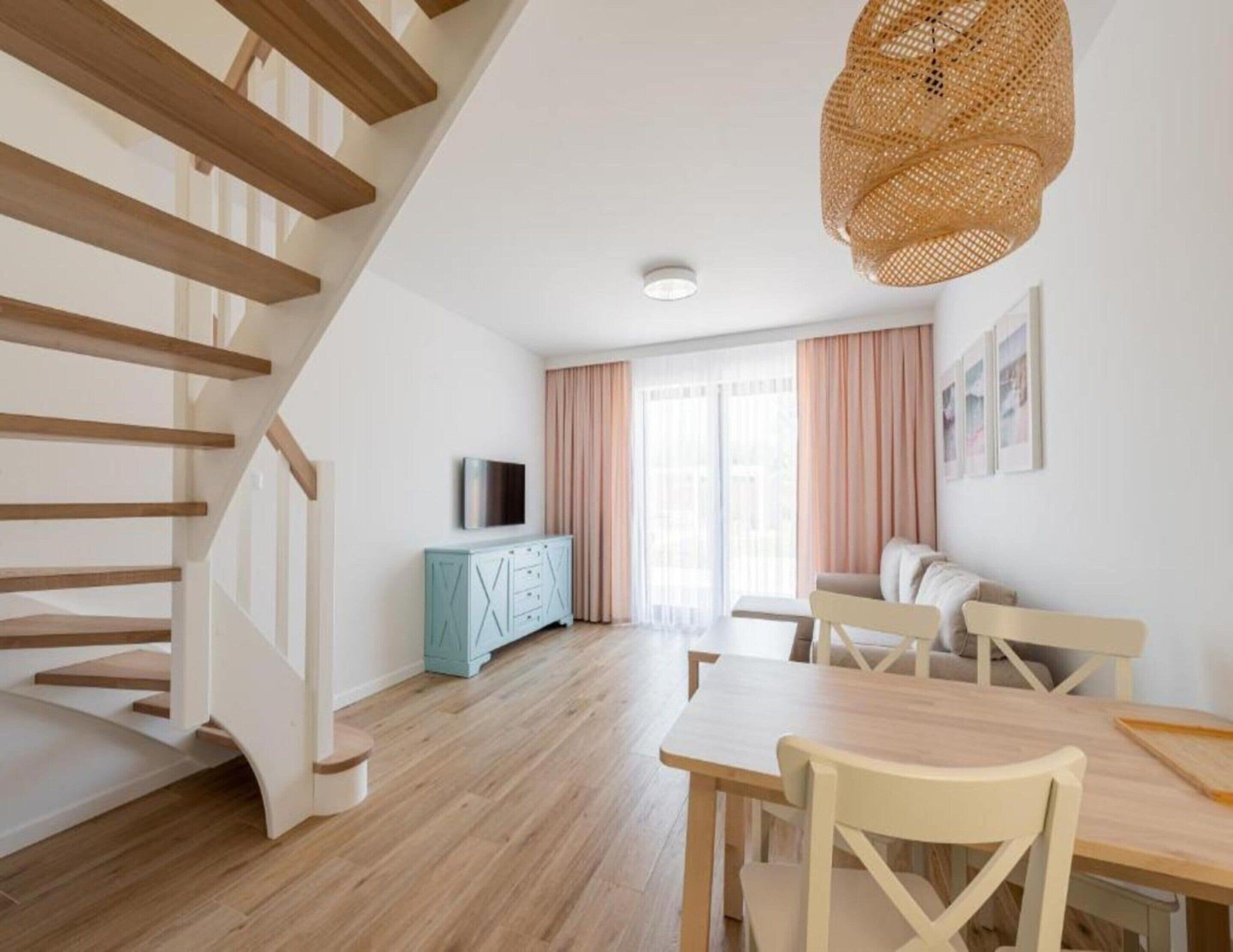 A modern living room with a staircase, wooden flooring, a dining area, and a television on a cabinet.