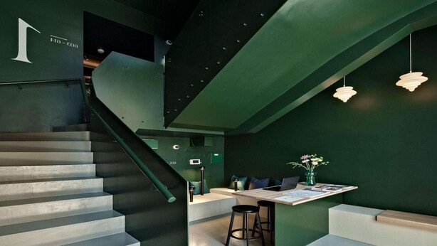 Ein modernes Interieur mit einer Treppe, einem Schreibtischbereich mit einem Laptop und einer grünen Wand.