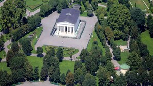 Eine Vogelperspektive eines großen, rechteckigen Gebäudes mit einem zentralen Innenhof, umgeben von gepflegten Gärten und Wegen.