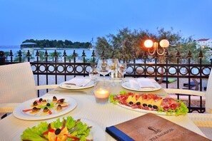 A table set for dinner with plates of food, glasses, and a candle, overlooking a body of water. - Apartment on Ugljan Island by Sandy Beach (Preko)