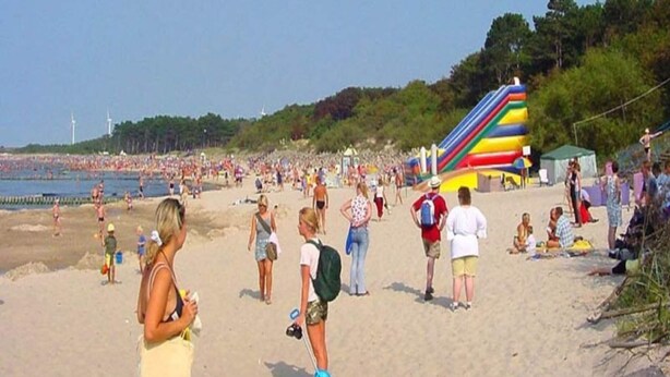 A crowded beach with people walking and sunbathing, a large inflatable slide, and a clear sky. - Apartment in Darlowko Near Beach & Water Park (Darlowo)