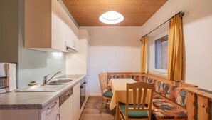 A compact kitchen with a sink, stove, and cabinets. There is a dining area with a table and chairs, and a window with curtains. - Apartment in Milders Near Stubai Glacier (Neustift Im Stubaital)