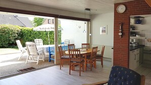 A dining area with a table and chairs, a blue chair, and a kitchen area with cabinets and a clock. - Doppelhaushhlfte in Burhave (Butjadingen)