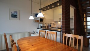 A dining area with a wooden table and chairs, a kitchen with white cabinets, and pendant lights. - Doppelhaushhlfte in Burhave (Butjadingen)