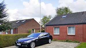 A black BMW parked in front of a red brick house with a paved driveway and a hedge. - Doppelhaushhlfte in Burhave (Butjadingen)