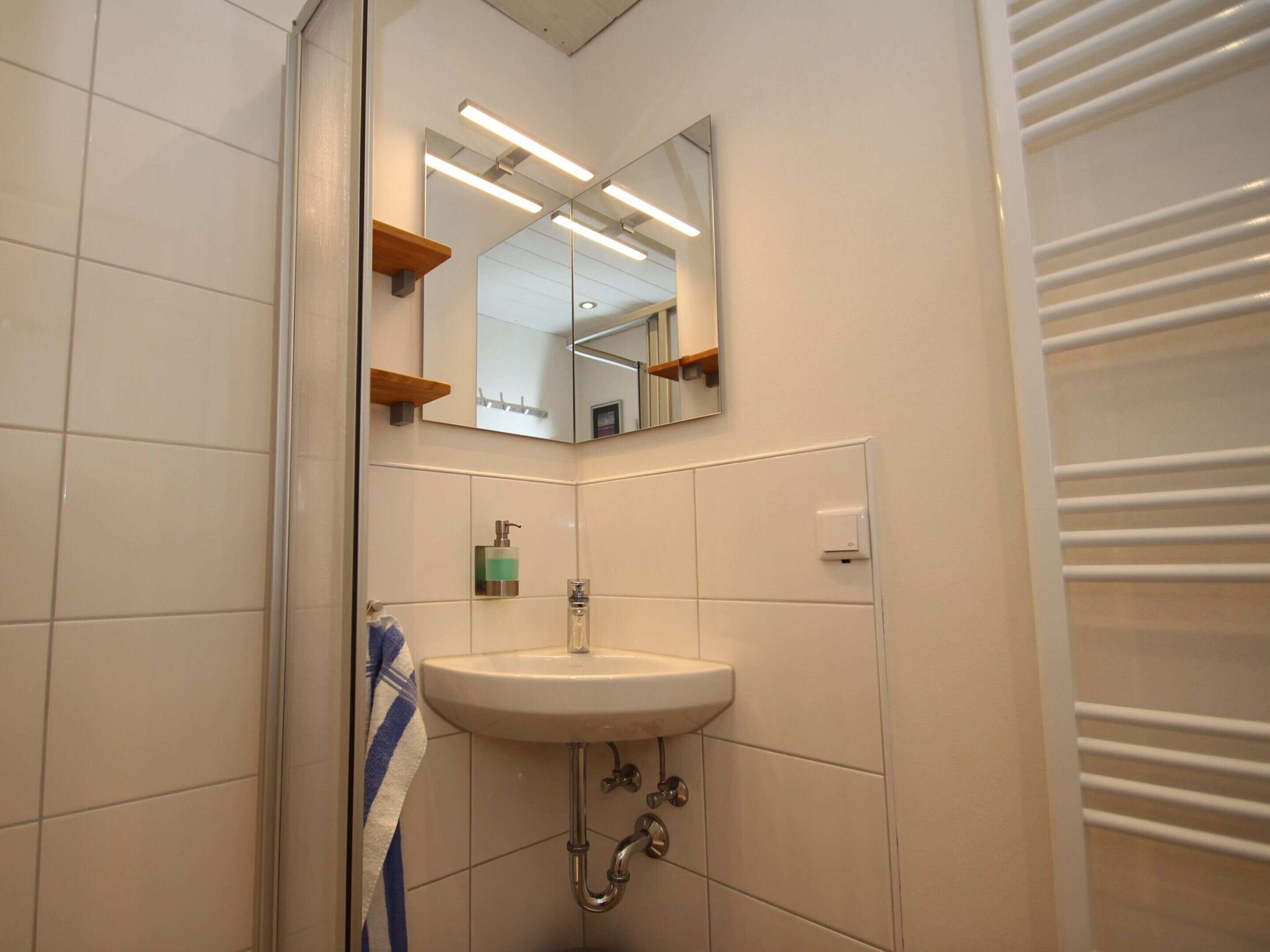Un baño con lavamanos blanco, espejo y toallero.