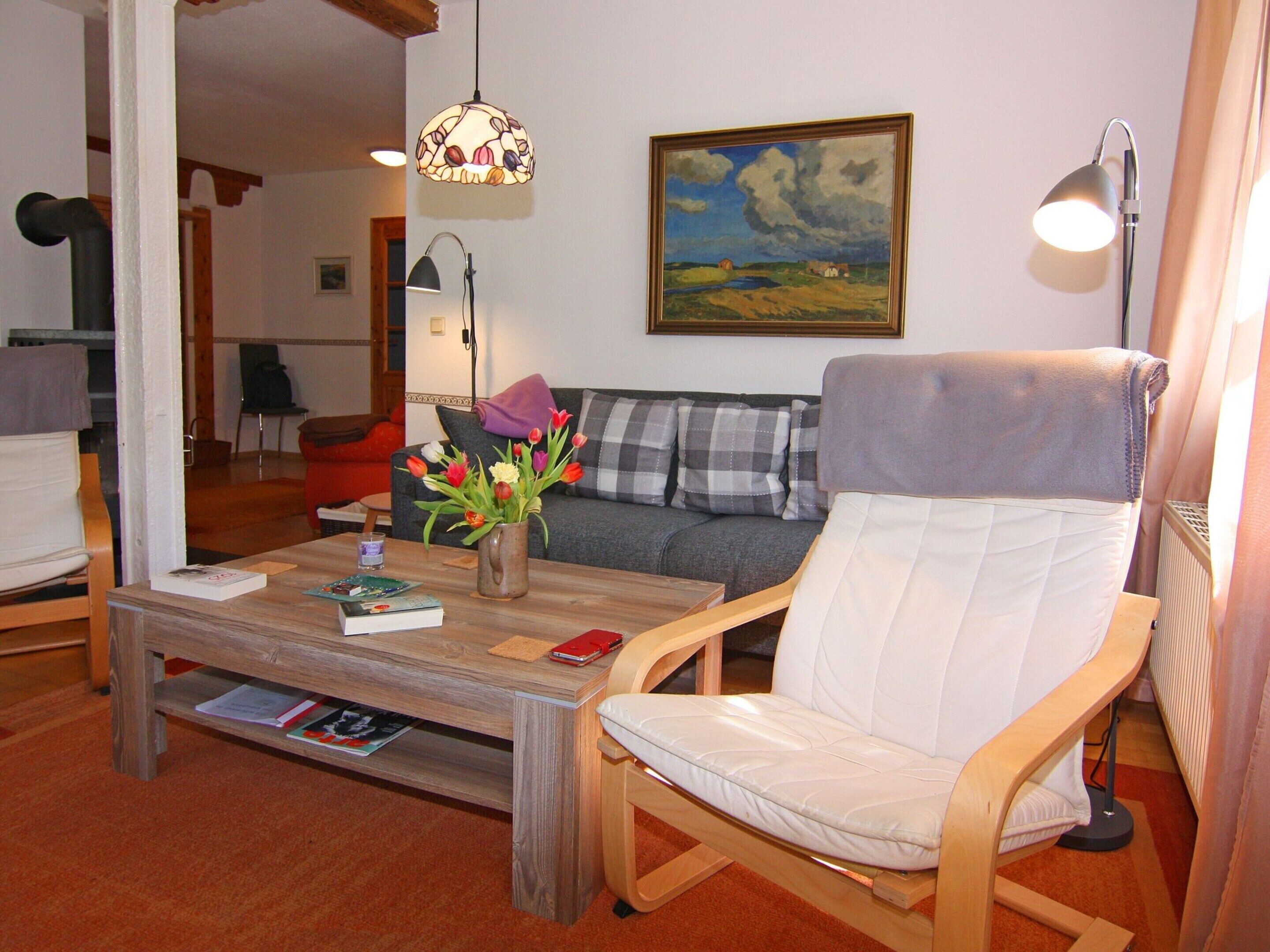 A living room with a wooden coffee table, a white armchair, a grey sofa, a painting on the wall, and a hanging light fixture.