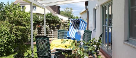 An outdoor patio with a table and chairs, a covered area, and a garden.
