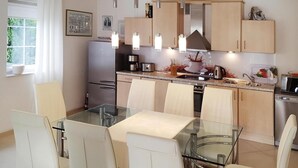 Une cuisine moderne avec une table à manger en verre, des chaises de couleur beige, des appareils électroménagers en acier inoxydable et des luminaires suspendus.