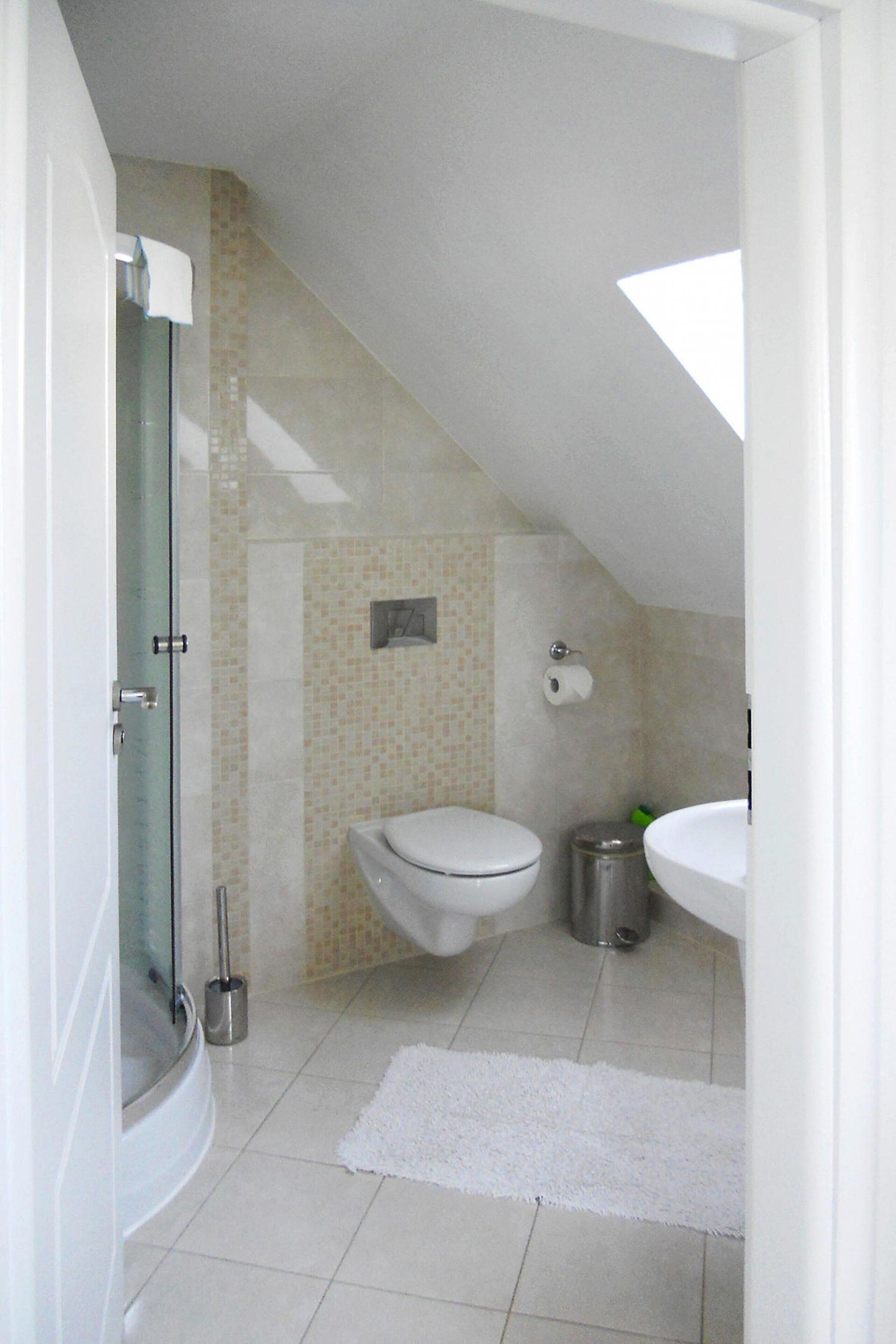 A bathroom with a glass shower enclosure, a toilet, a sink, and a trash can.