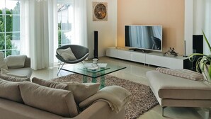 Un salon moderne avec une table basse en verre, des canapés de couleur beige, un téléviseur à écran plat et une décoration minimaliste.