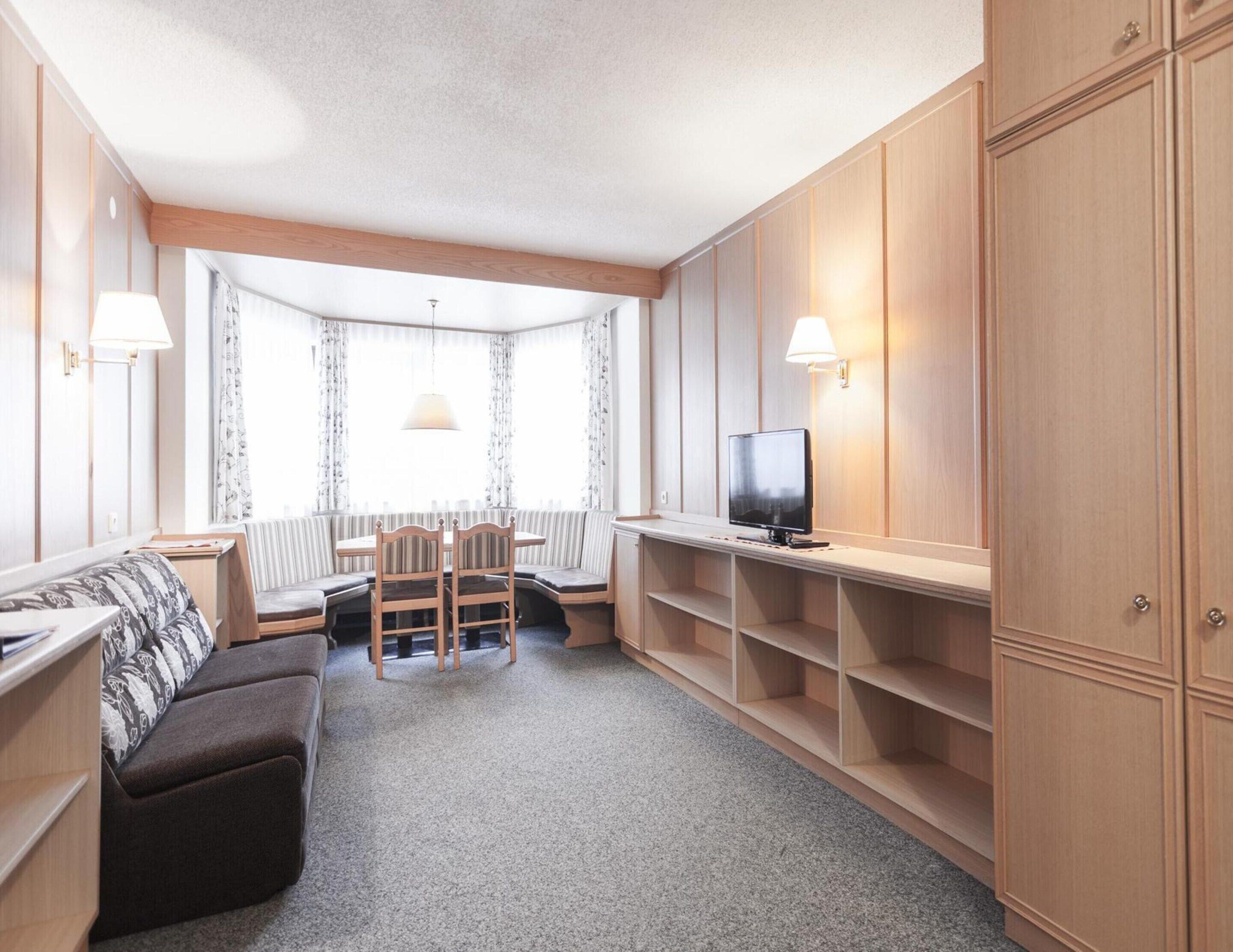 Un espace de vie compact comprenant un canapé, une table à manger avec des chaises, un téléviseur et des armoires encastrées en bois.