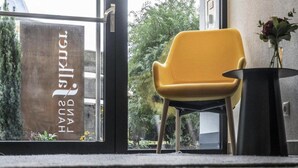 Une chaise jaune dans une pièce avec une fenêtre sur laquelle on peut lire le texte « HAND LAND ».