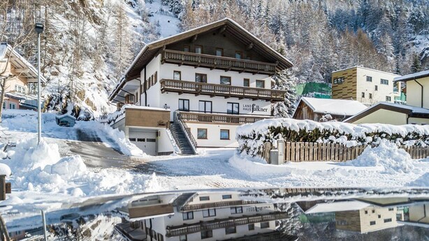 Un immeuble à plusieurs étages doté d’un balcon, entouré d’arbres couverts de neige et dont le reflet se mire clairement dans l’eau.