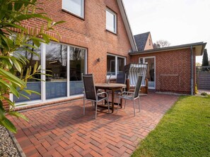 Une maison en briques avec un patio comprenant une table et des chaises, une porte-fenêtre coulissante et un petit jardin.